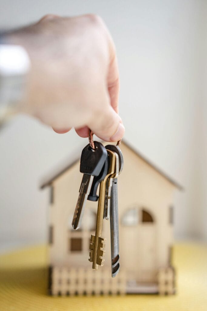 Hand met huissleutels voor een miniatuurwoning als symbool voor hypotheek en woningkoop.