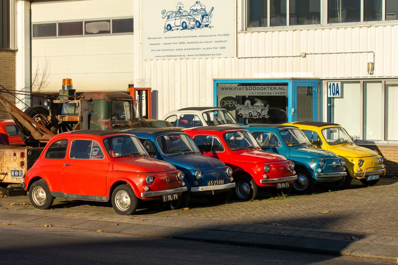 Row of colorful vintage Fiat 500 cars parked in sunlight outside a garage.