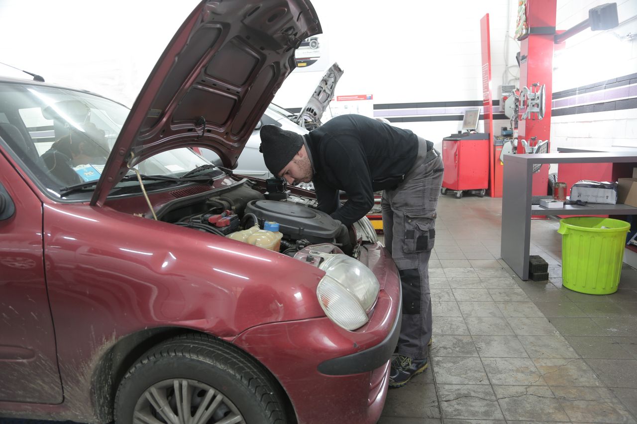 our-story Mechanic performs engine inspection on a red car indoors, in a garage workshop.