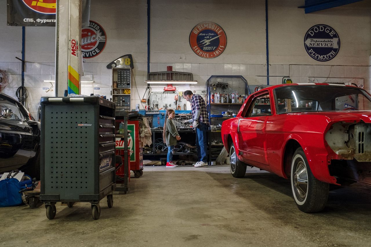 about-us A father and daughter spend quality time together in a bustling auto repair shop, fixing cars.
